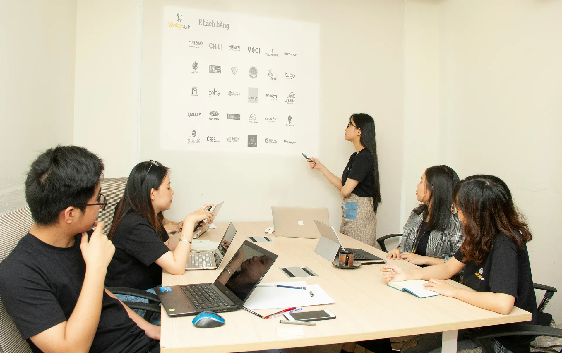 Team meeting in a modern office with a presenter showing client logos on a screen