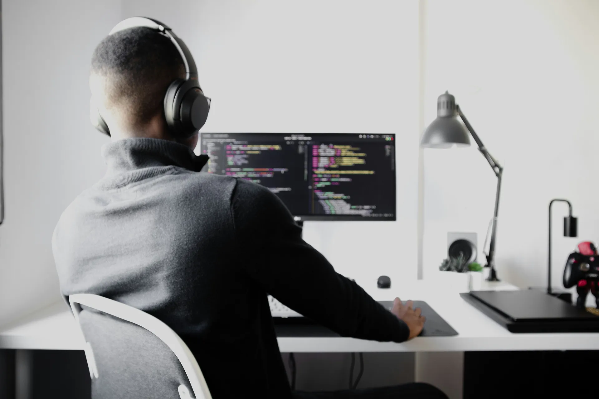 Software developer wearing headphones coding on a desktop computer in a minimalist workspace