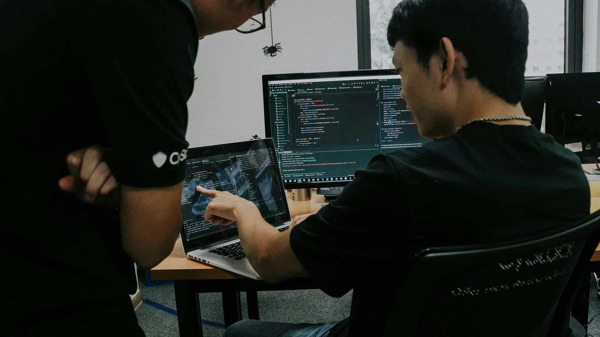 Two software developers collaborating and reviewing code on laptop and desktop screens