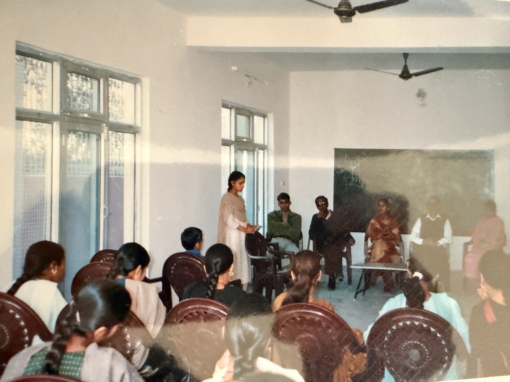 Historic family photograph taken inside the Republic College of India at Jahu, showing three people seated behind a desk.