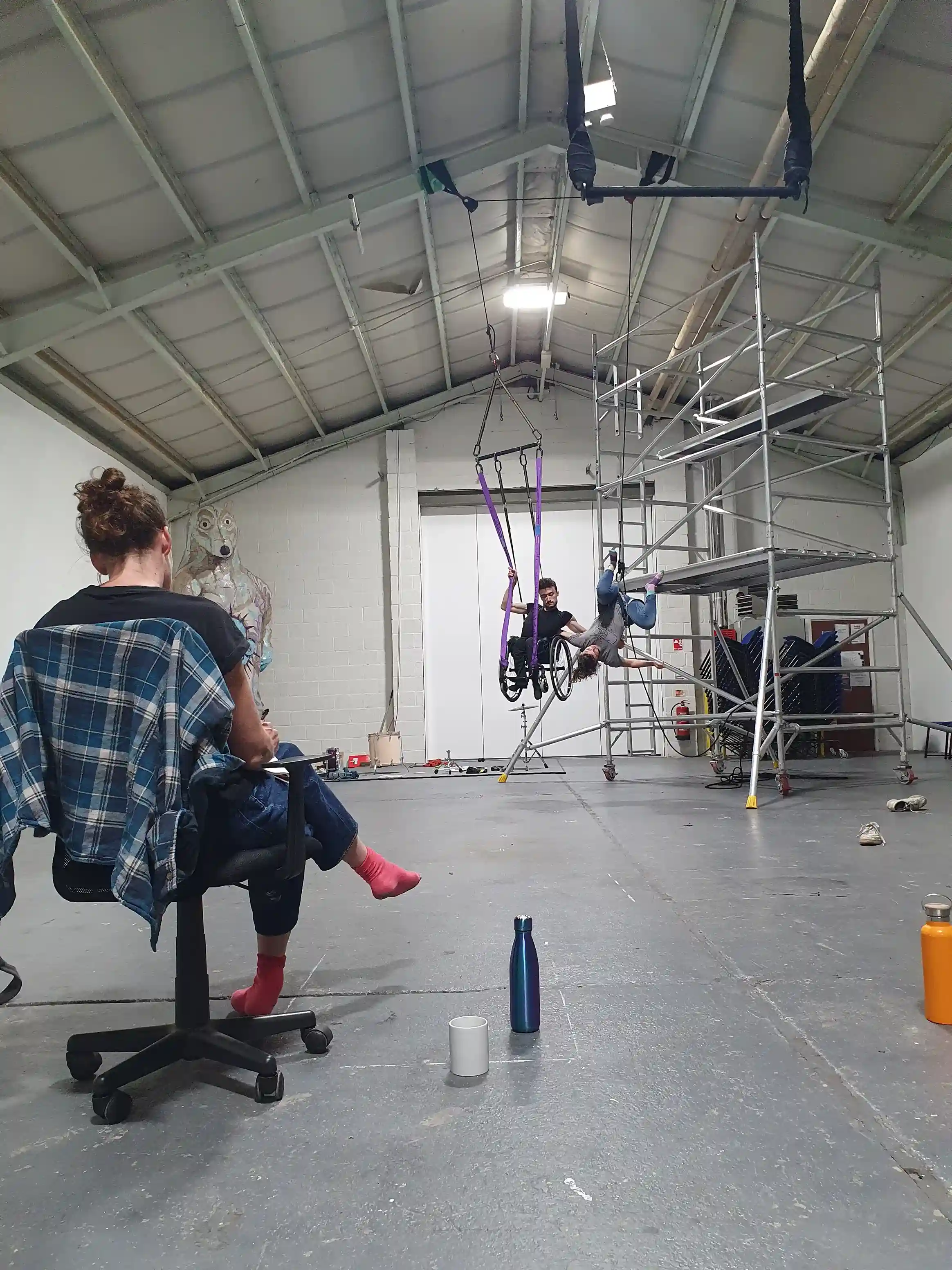 Jonny and Tilly are on a structure in the background of the image with the director sat on a chair in the foreground