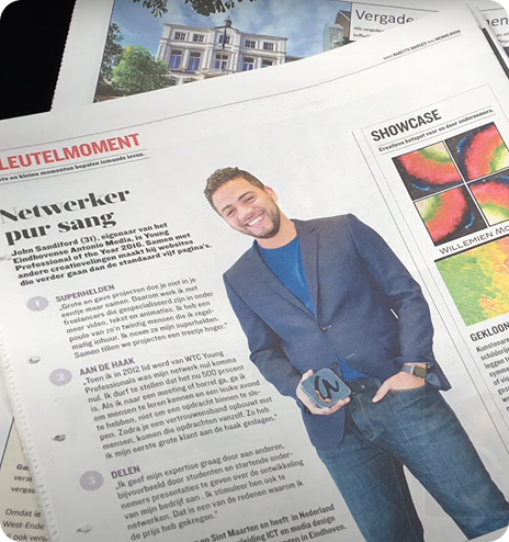 Smiling man with short hair and beard wearing a dark blue blazer and jeans, holding a small trophy, featured in a newspaper article titled 'Netwerker pur sang'.