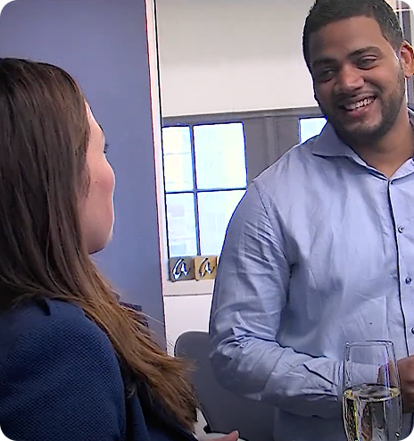 Two colleagues smiling and talking in an office with a glass of champagne on the table.
