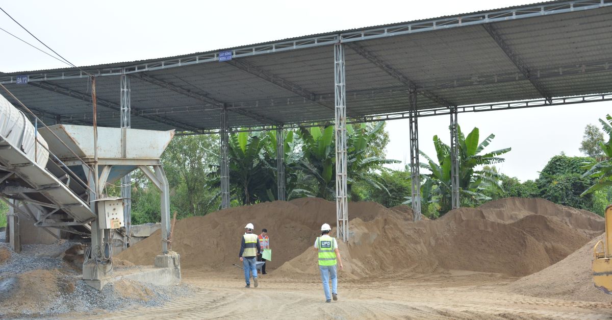 Industrial construction site with workers inspecting sand piles under metal roofing.