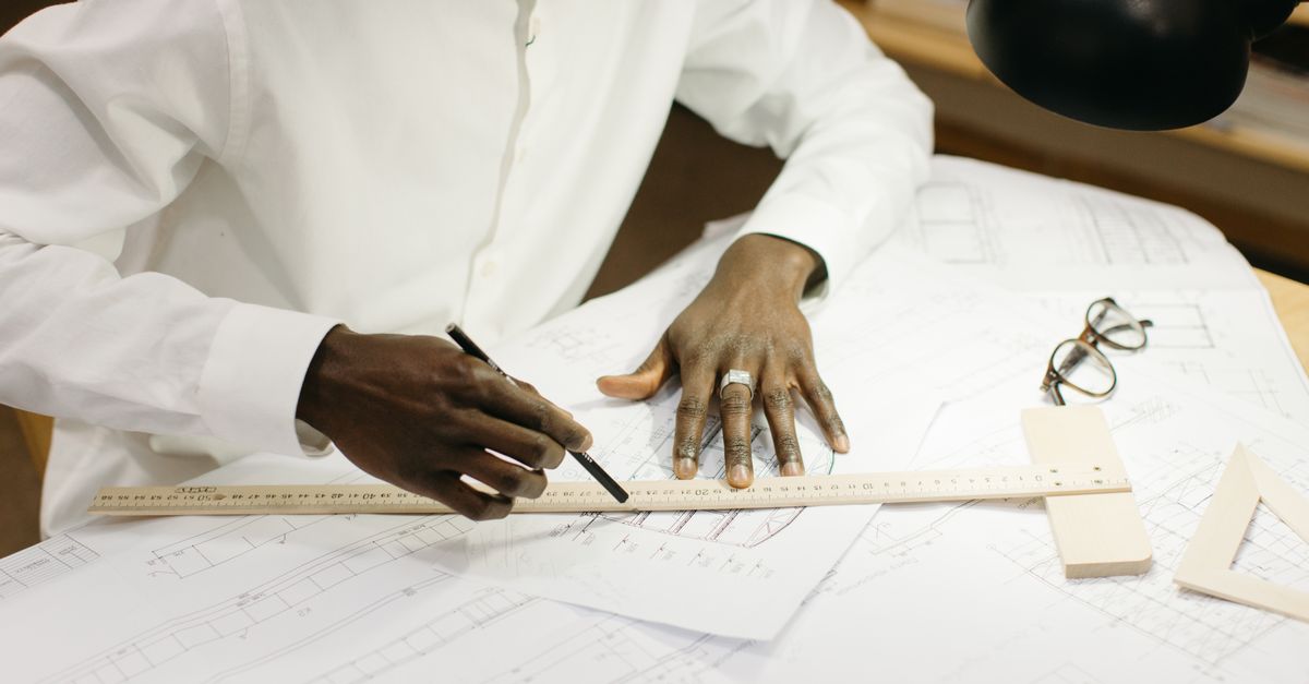 An architect diligently works on blueprints at a well-lit office desk with design tools.