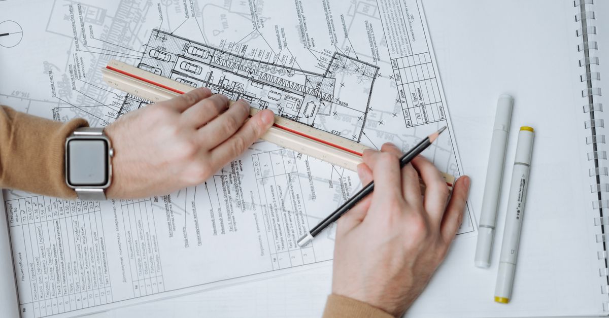 An architect uses a ruler and pencil on blueprints, showcasing workspace and planning.