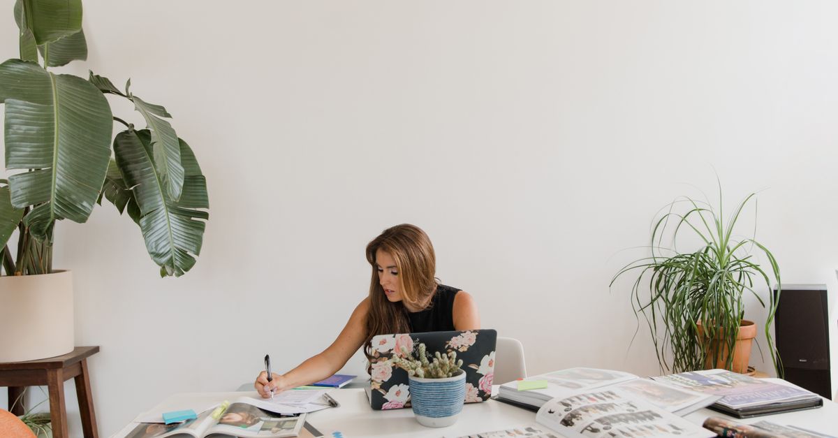 Contemporary home office setup featuring a woman working amidst lush houseplants and design magazines.