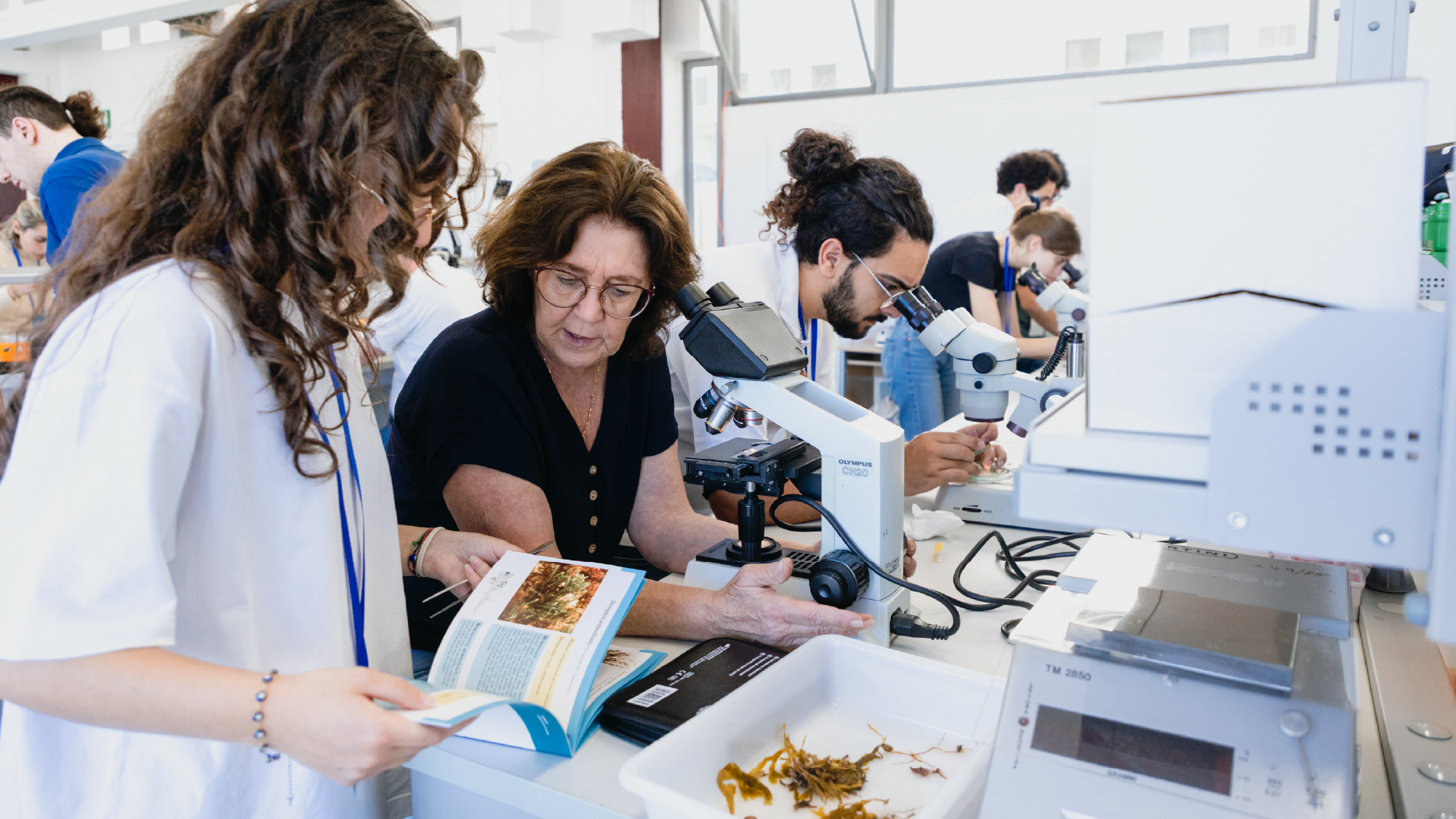 Docente e studenti in laboratorio con microscopi e manuale durante un workshop BioDiv School, SevenApp