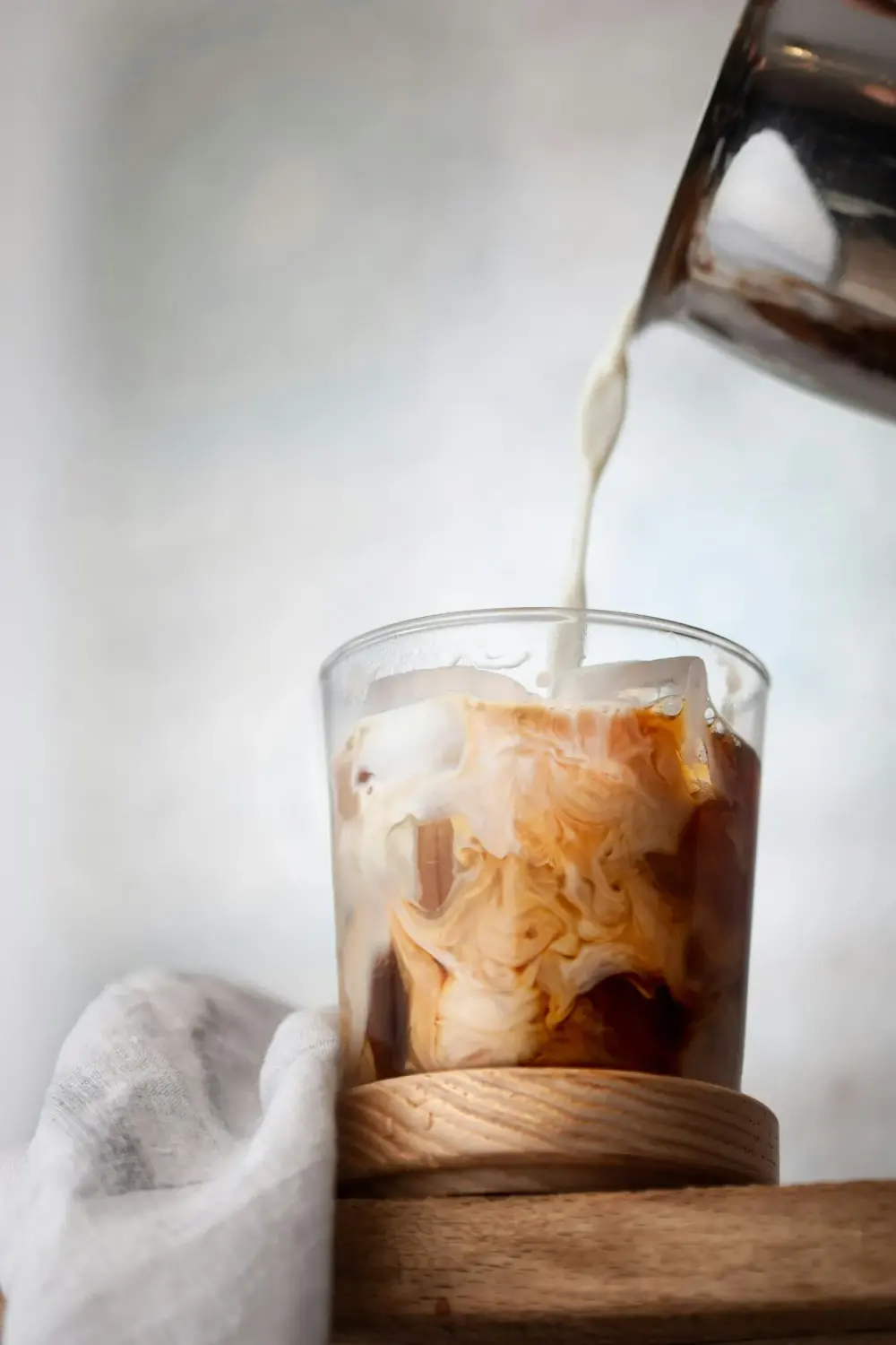 Milk being poured into a glass of iced coffee