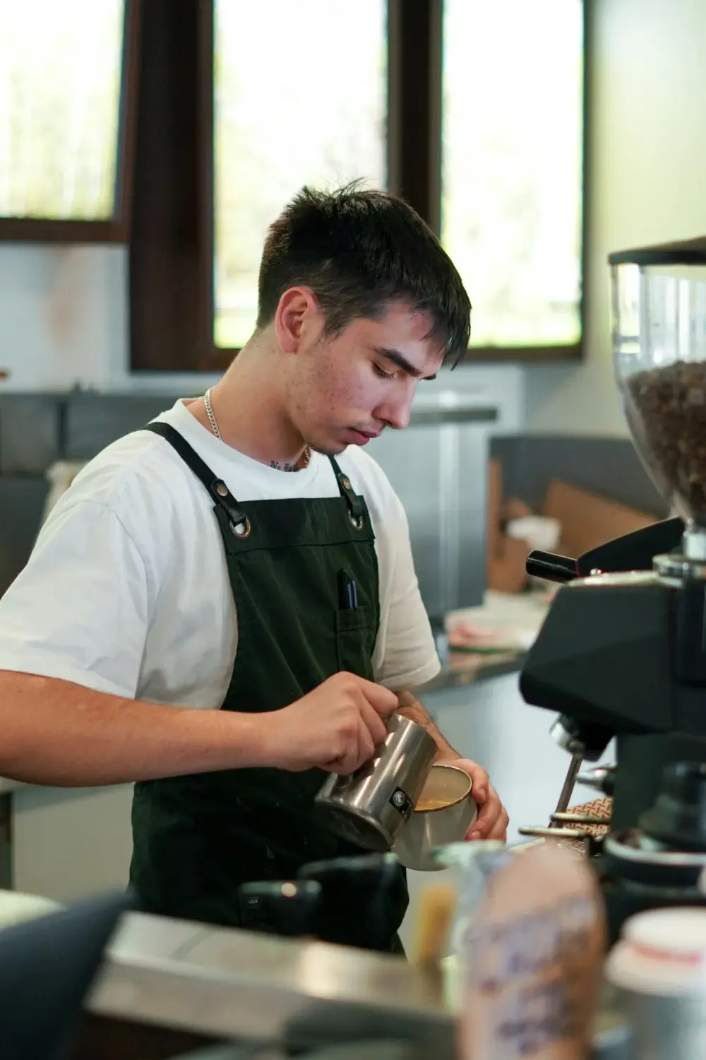 A barista steaming milk behind a coffee shop counter