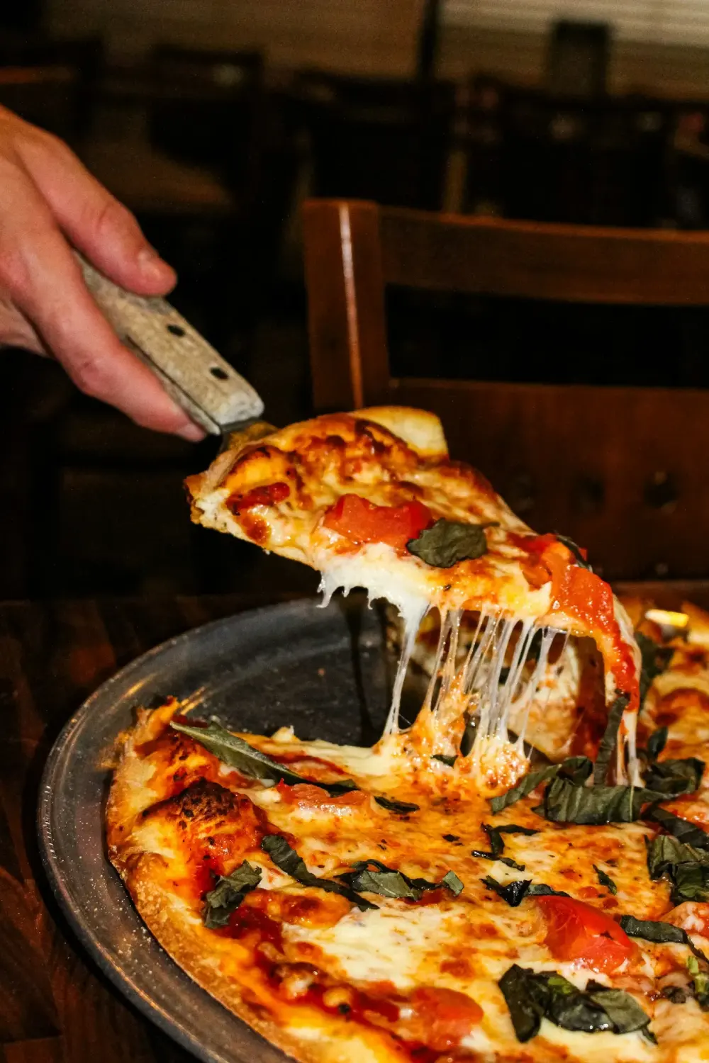 A slice of wood-fired pizza being lifted, cheese stretching
