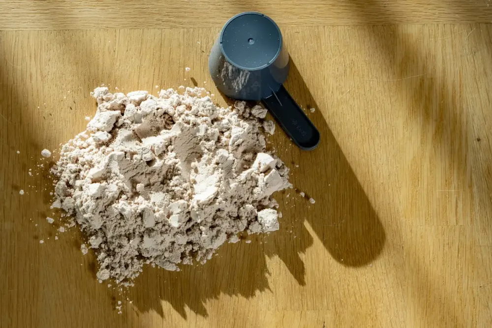 A scoop of protein powder on a sunlit wooden table