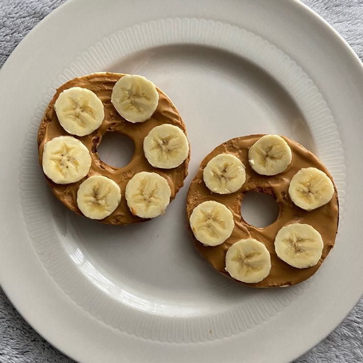 This may contain: two bagels with peanut butter and banana slices on them sitting on a white plate