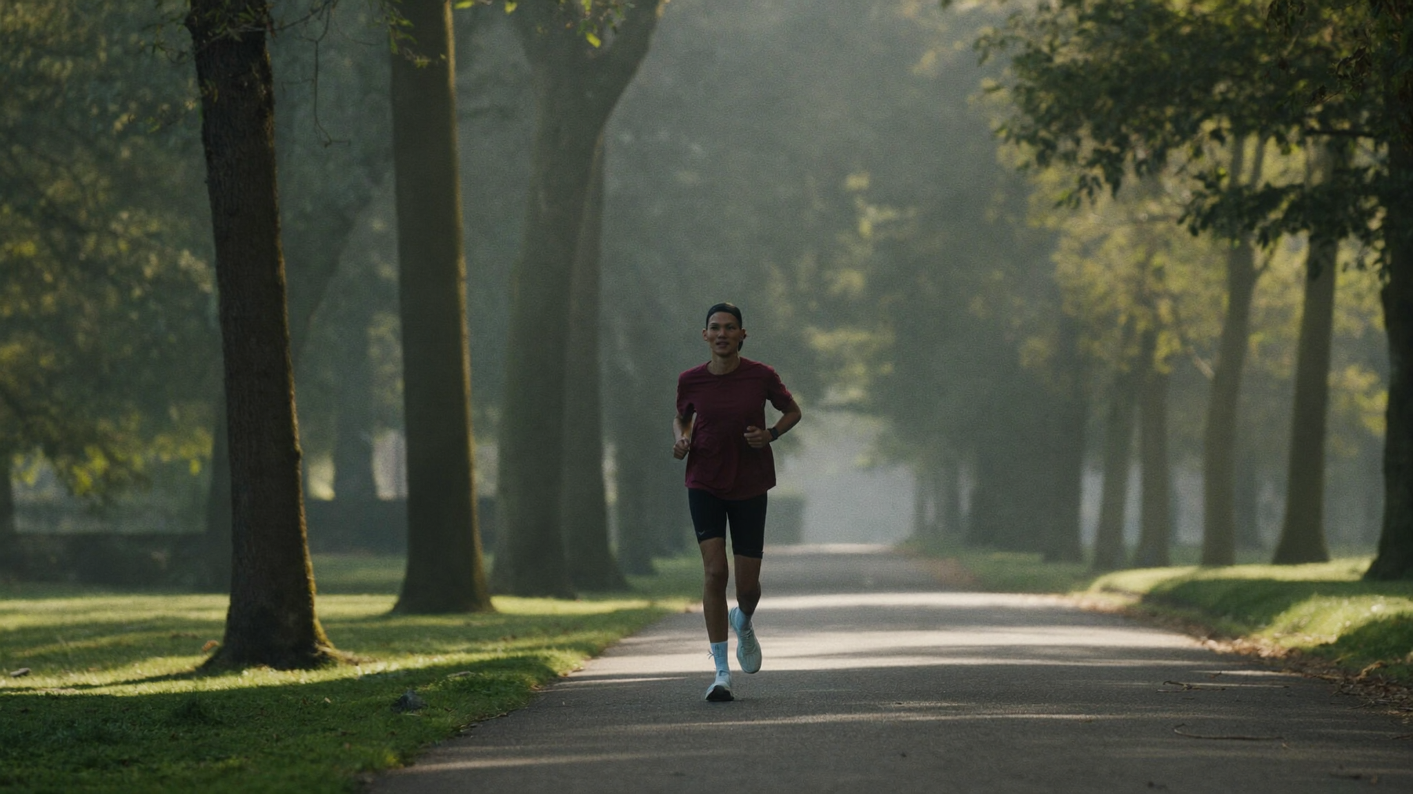 A runner jogging on a tree-lined road in soft morning light