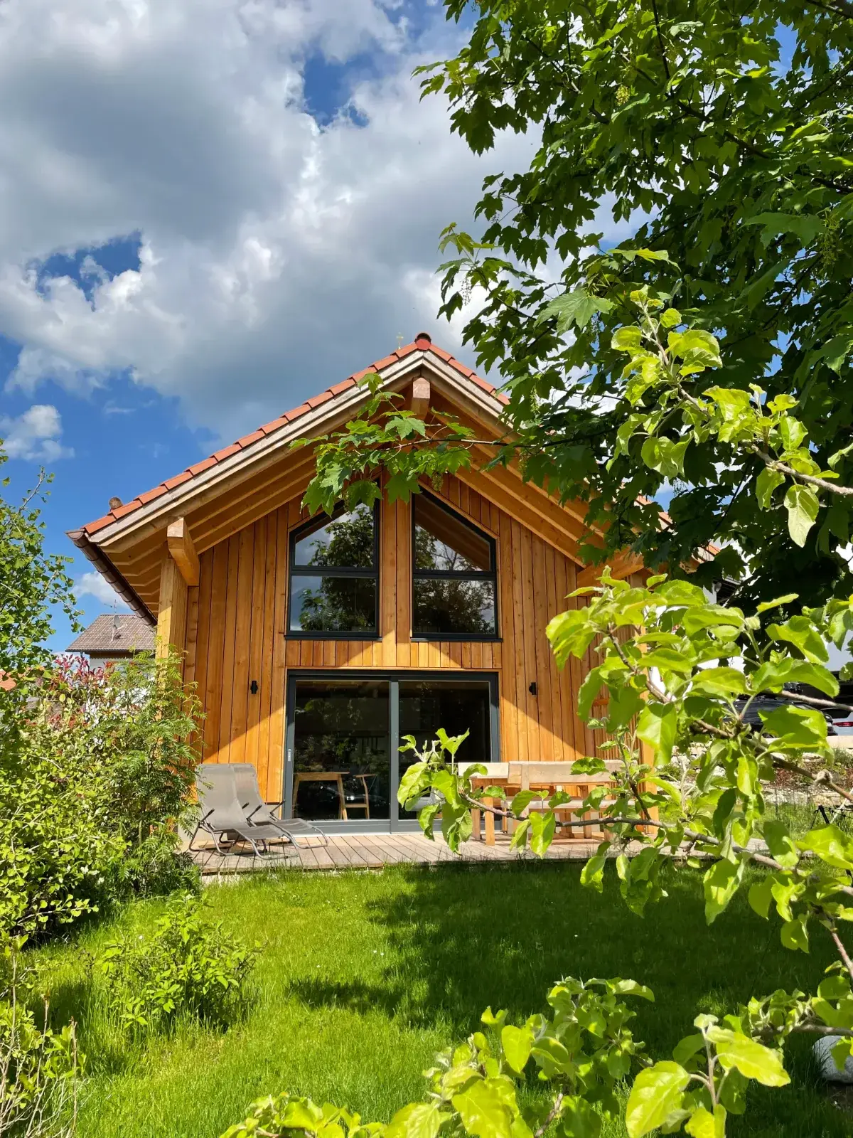 Holzchalet mit großen Giebelfenstern unter dem Ahorn