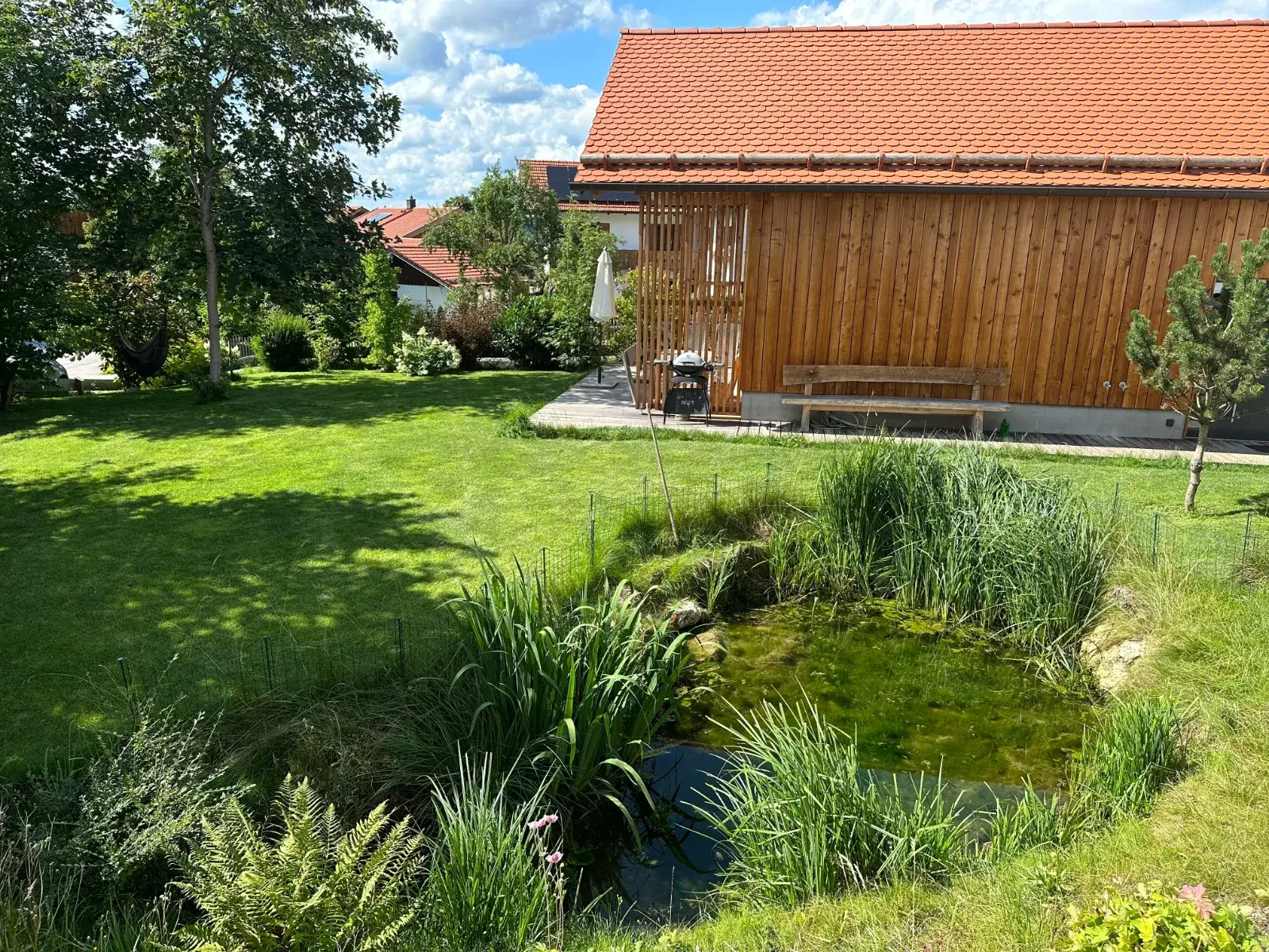 Naturteich im Garten, dahinter das Chalet mit Grill und Sitzbank