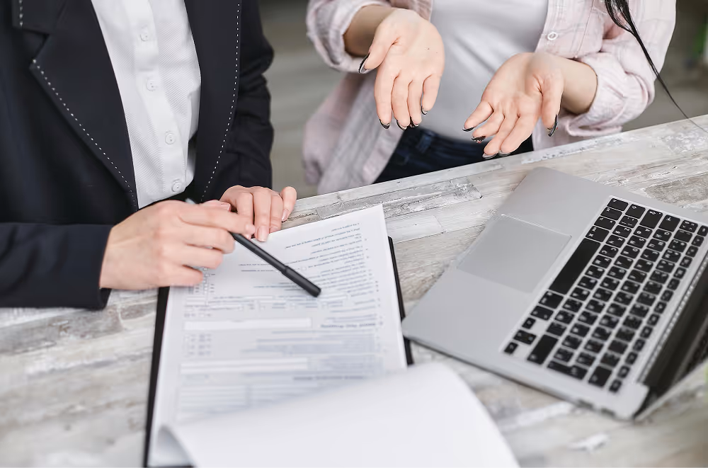 people sitting next to laptop and clipboard with pen