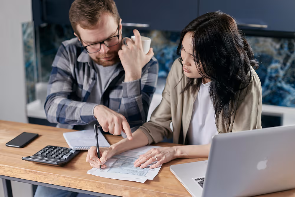 couple filling out form next to calculator and laptop