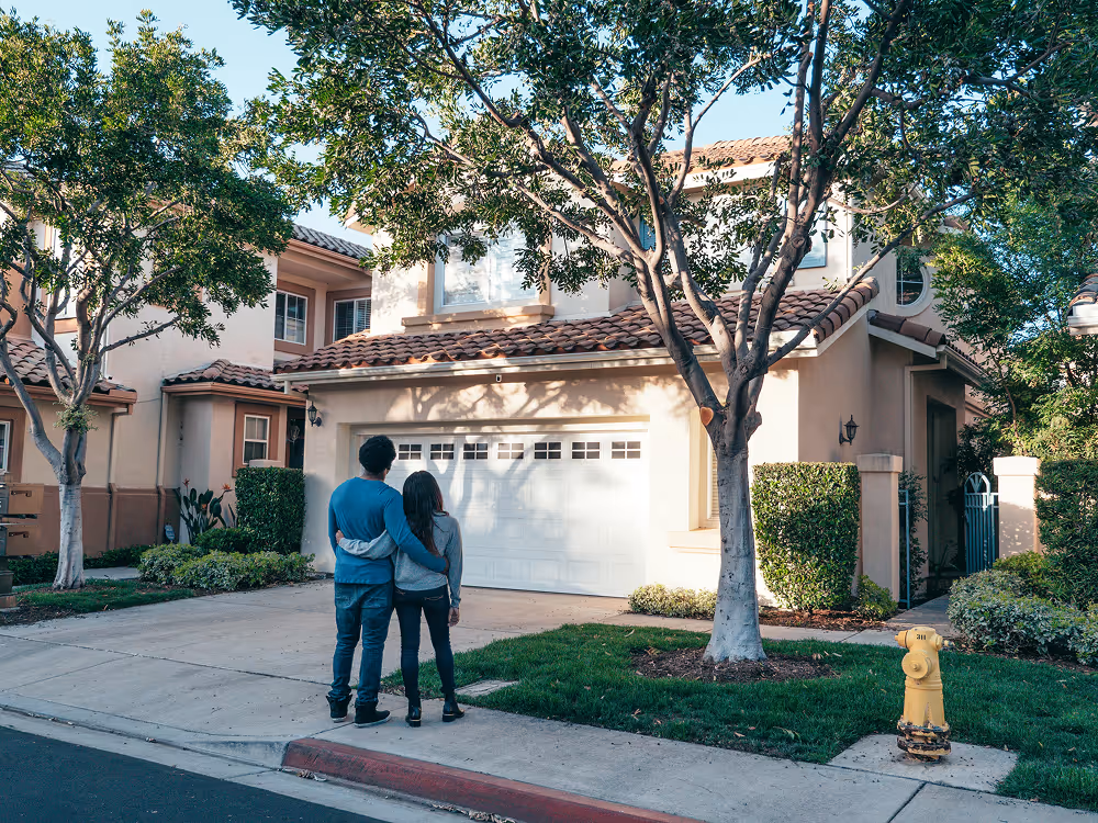 a behind shot of a couple standing in driveway looking at new home