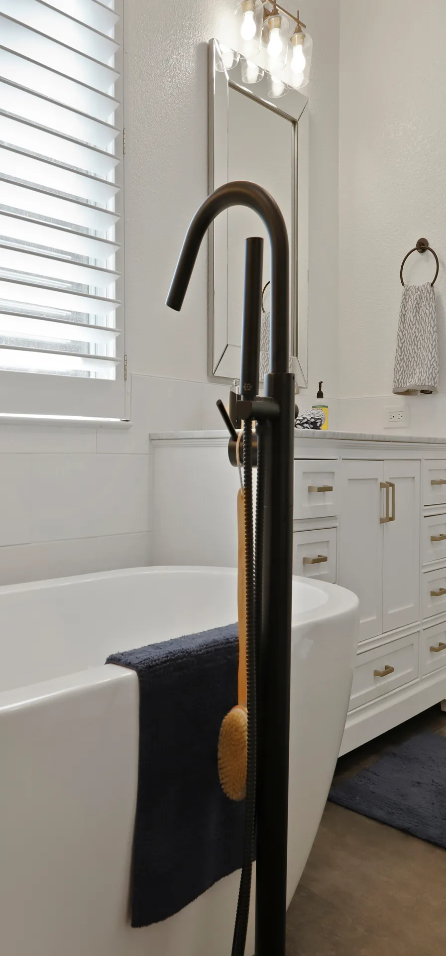 Modern bathroom with a freestanding black tub faucet, white bathtub, navy towel, and white vanity with gold handles.