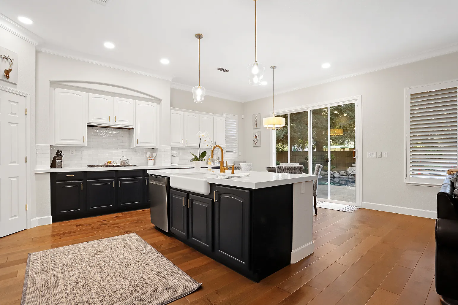 A beautiful wide angle shot of a kitchen with an island, with wood floors, black lower cabinets, and white upper cabinets.