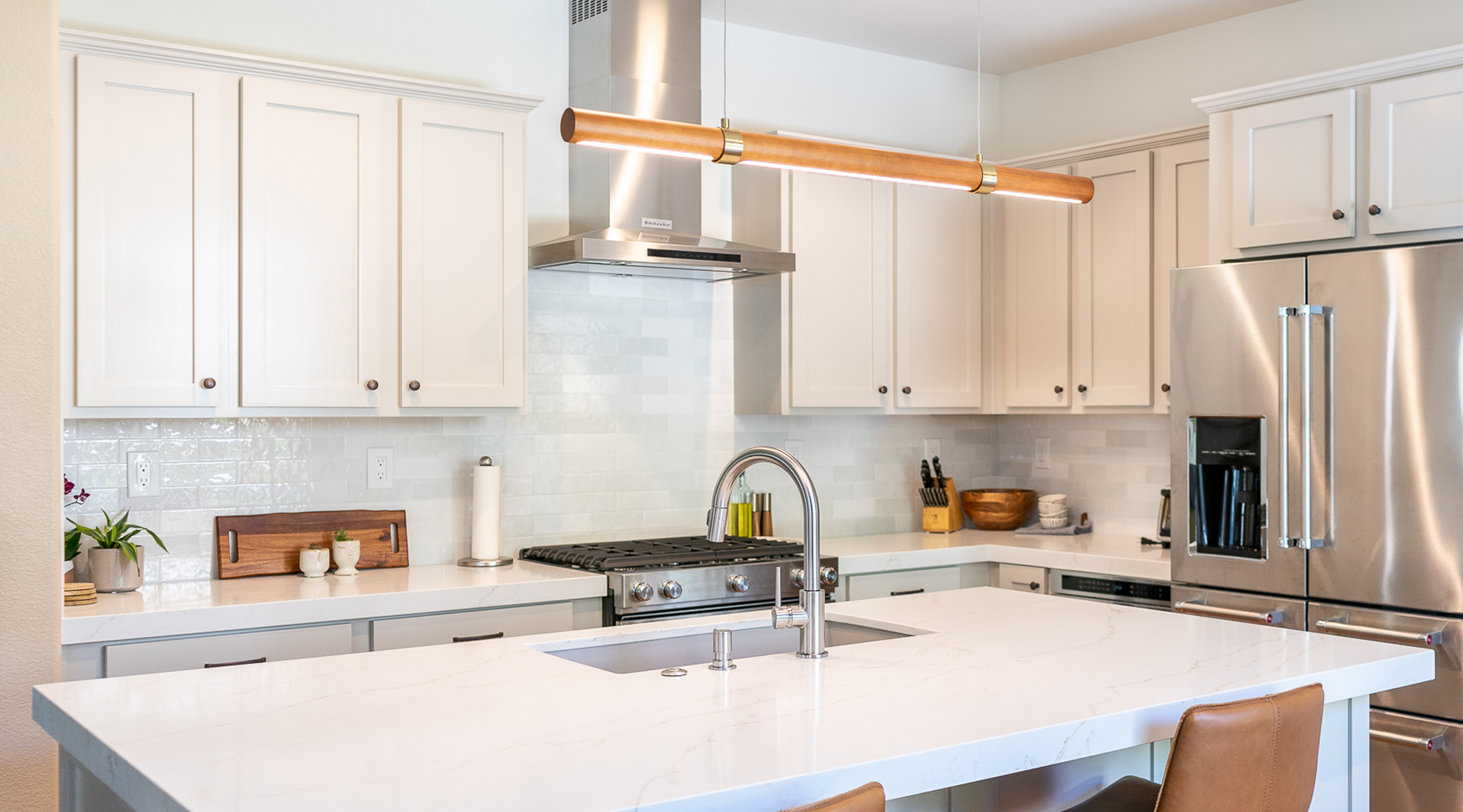 Modern kitchen with white cabinets, stainless steel appliances, marble countertop island, and a wooden pendant light.