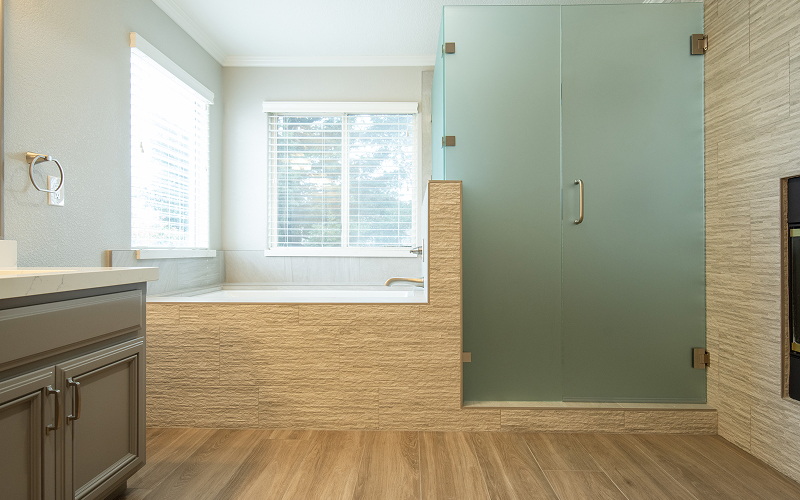 Modern bathroom with a built-in bathtub under two windows and a frosted glass shower enclosure.