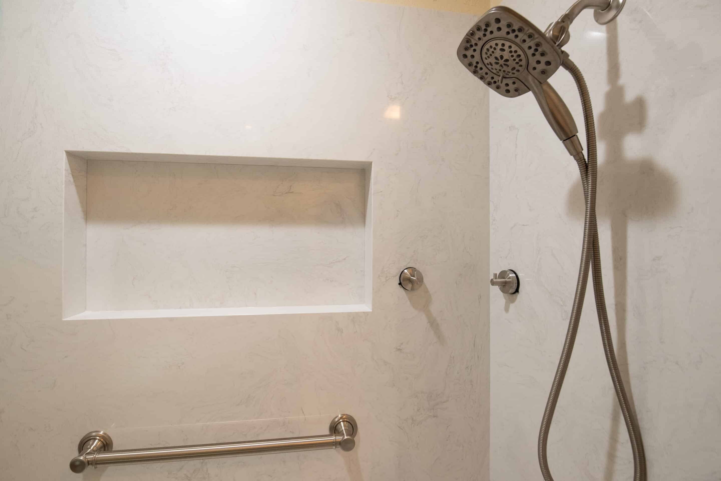 Modern shower area with a built-in empty niche, stainless steel grab bar, and adjustable handheld showerhead on a flexible hose.