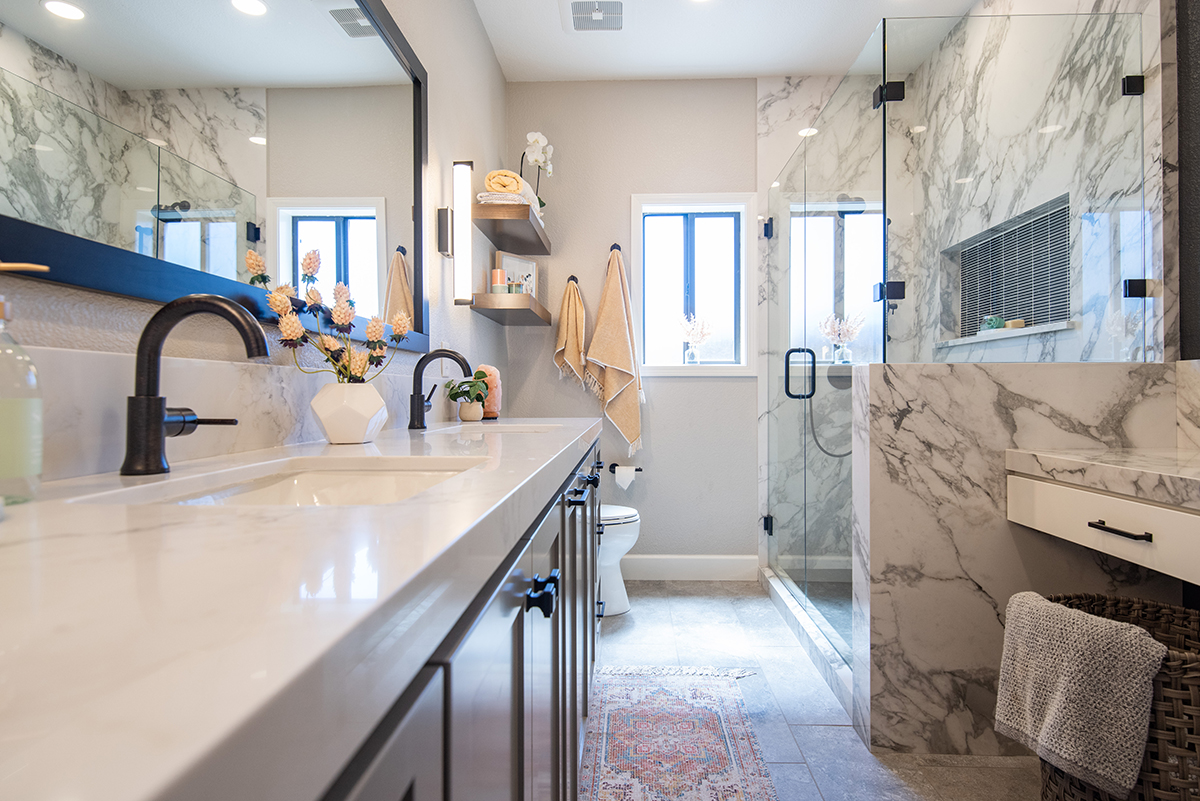 Modern bathroom with dual sinks, black faucets, marble countertops, glass-enclosed shower, and beige towels hanging near a window.