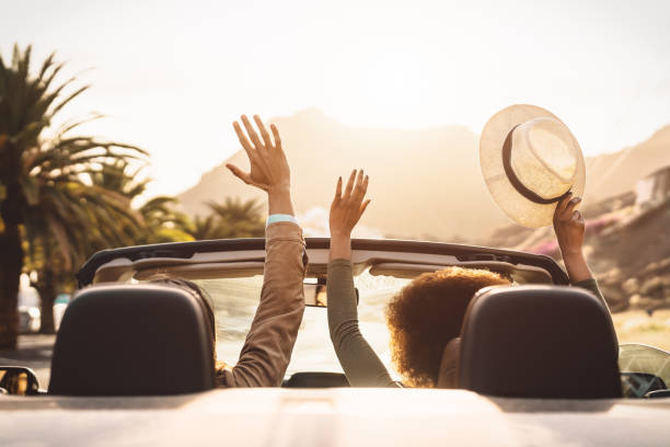 a couple in a convertible car with their hands raised going down the road