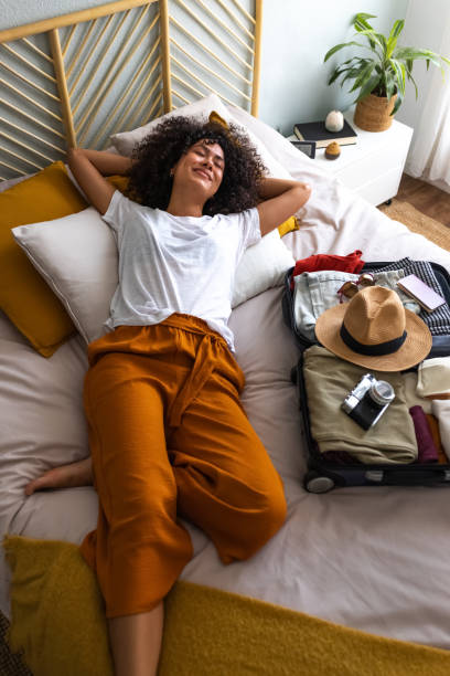 woman laying on a bed in orange pants after packing a suitcase for vacation