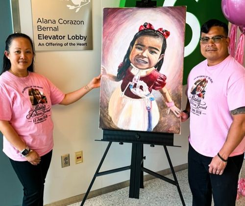 Two people with a painted portrait on an easel beside the Elevator Lobby dedication plaque