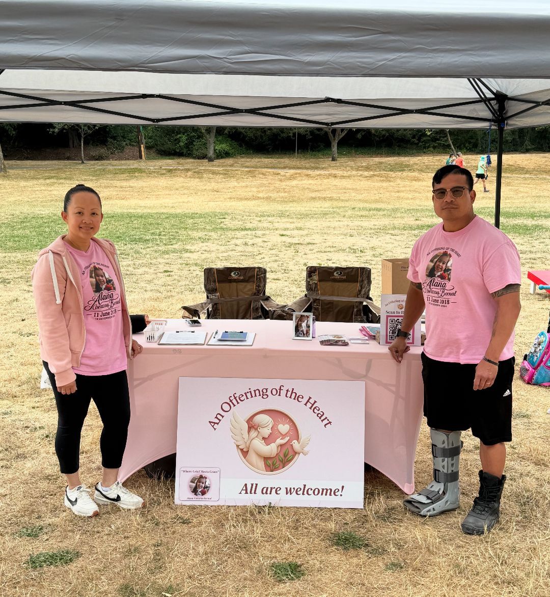 Two people at the An Offering of the Heart table with an All are welcome sign