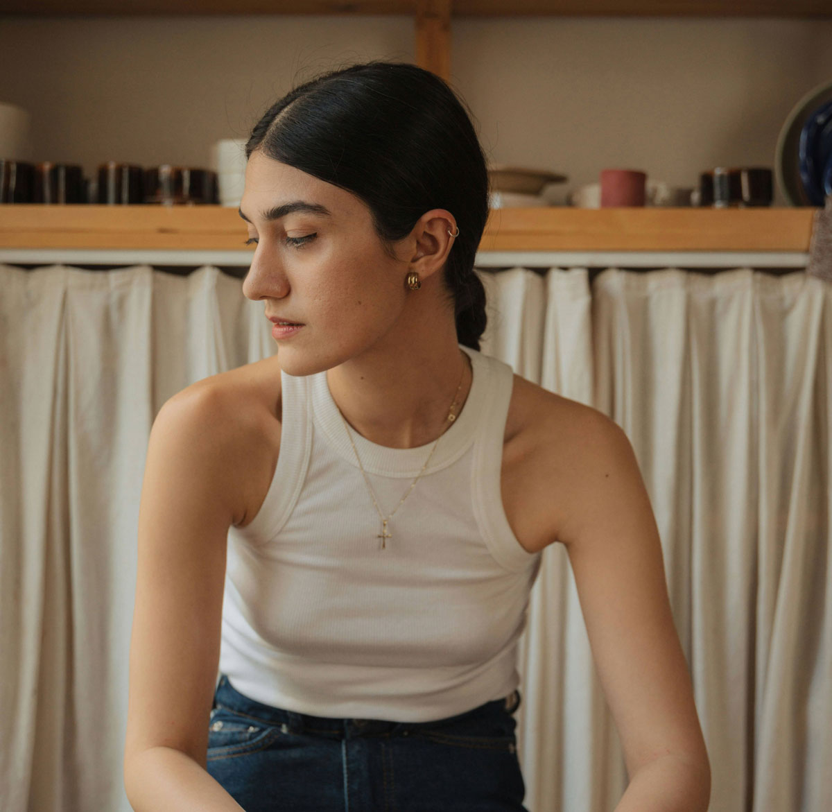 Woman in a yellow sweater holding a mug and looking out a window, reflecting during therapy