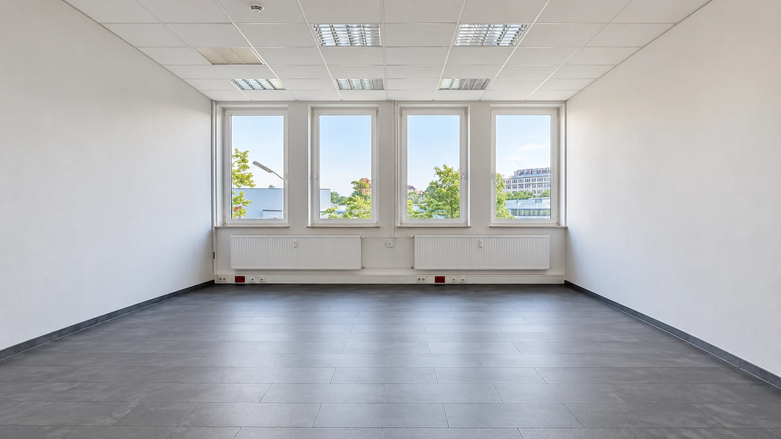 Large bright artist studio at GODU with four windows, white walls and dark tiled floor