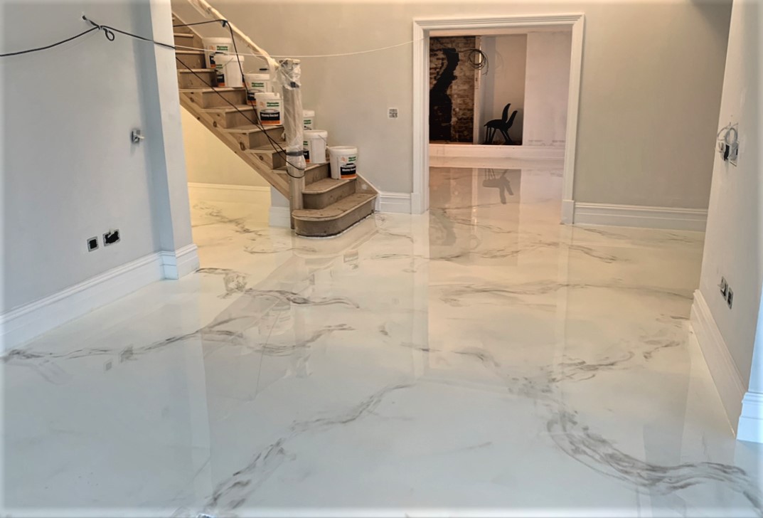 White marble-effect metallic epoxy floor in a home entryway, its gloss reflecting the staircase and the doorway beyond.