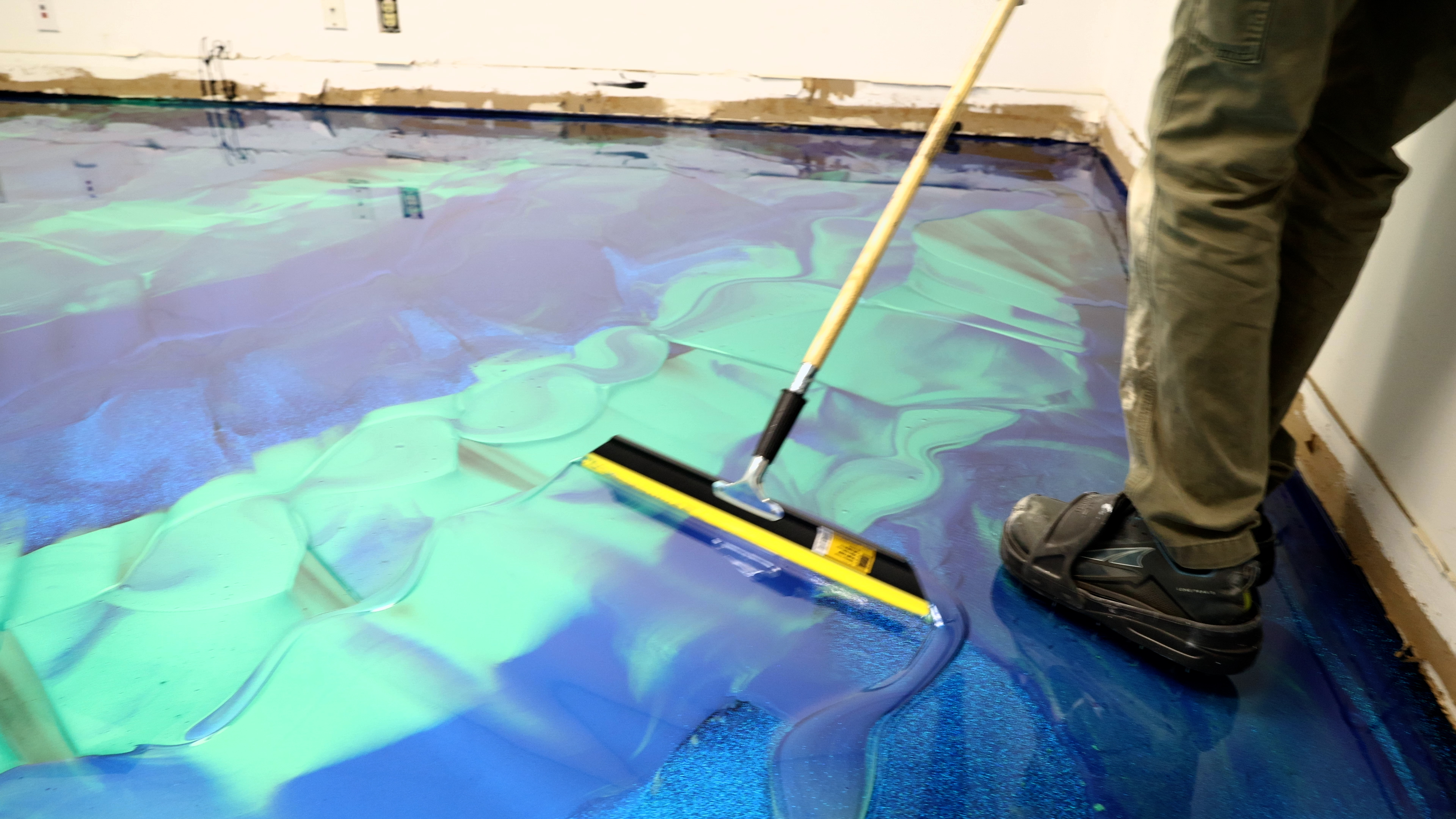 Installer spreading a blue and green metallic epoxy floor with a squeegee while the resin is still wet.