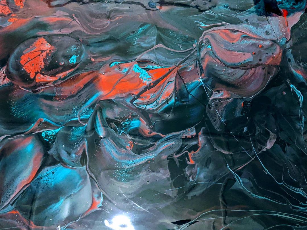 Close view of teal, orange and black metallic pigments swirled together across a poured epoxy surface.