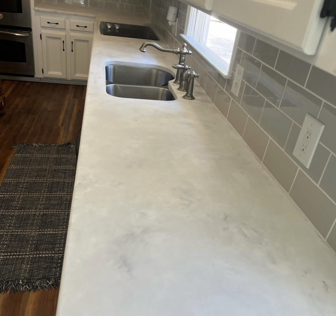 White marble-effect epoxy countertop running the length of a kitchen wall, with an undermount double sink and grey subway tile backsplash.