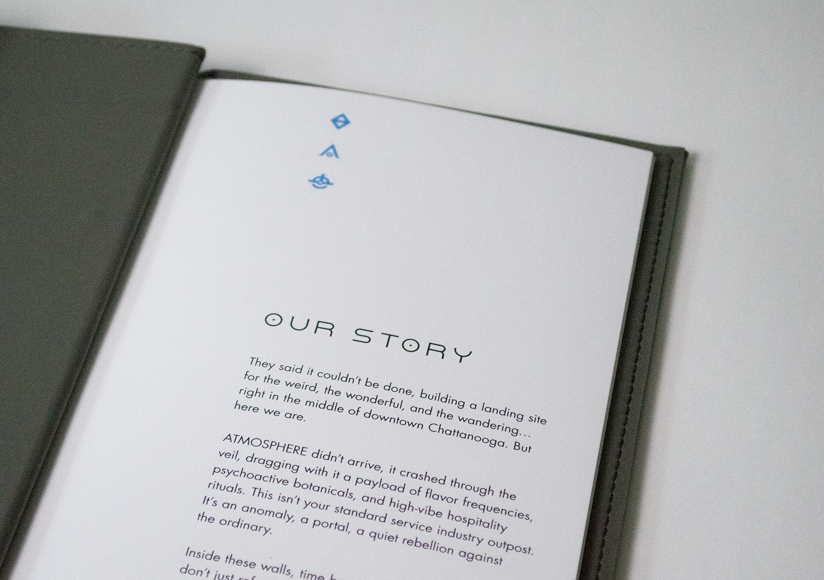 Introduction page of the cocktail menu with text that is titled "Our Story". The page uses alien symbols from the ATMOSPHERE brand identity.