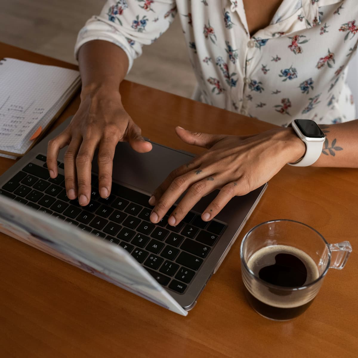 Woman typing on laptop at wooden desk with coffee and notebook for doula business management