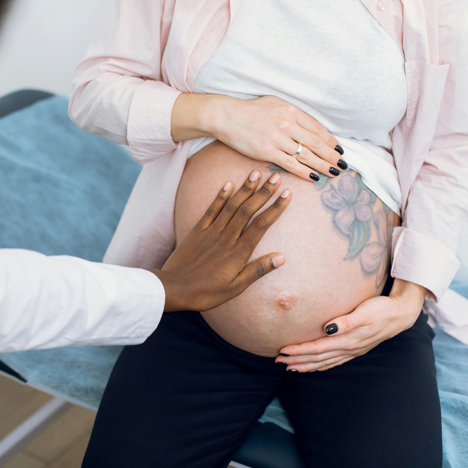 Doctor's hand on a pregnant belly with a tattoo