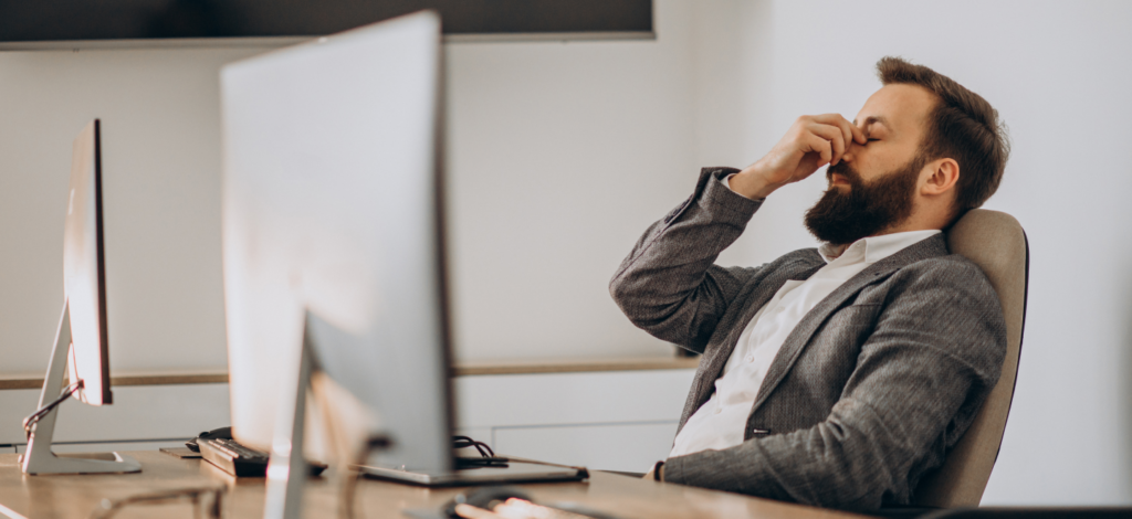 Businessman in a suit at an office desk appearing overwhelmed or exhausted