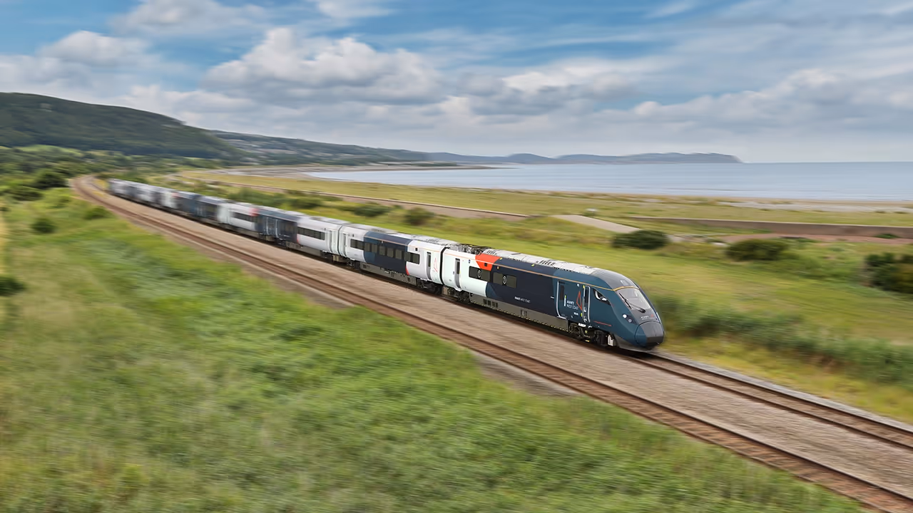 Train travelling on tracks with grass around it and view of the sea in the distance