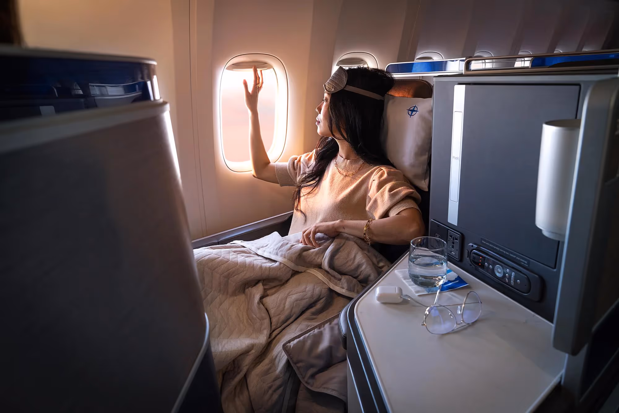 Woman with a sleep mask on her forehead, looking out the window of a United Airlines plane