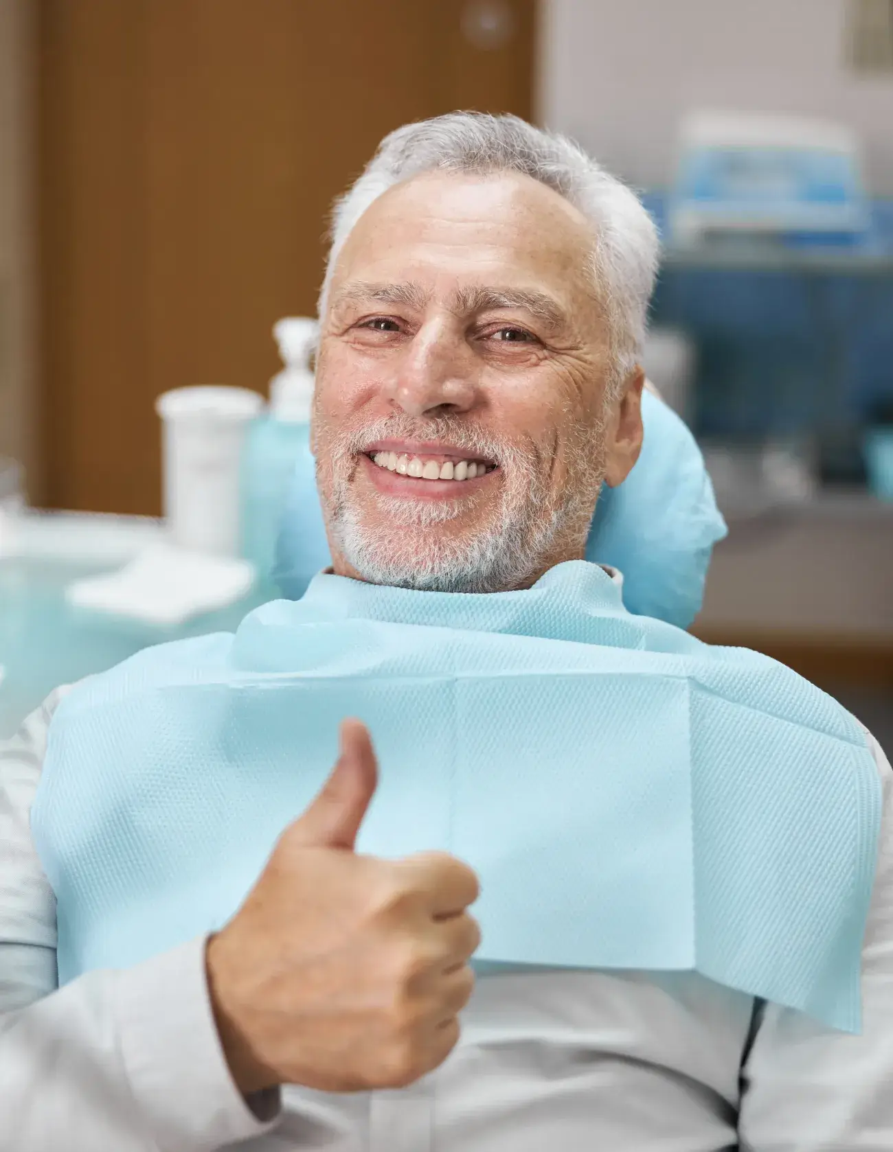 Elderly man sitting in a dental chair, smiling and giving a thumbs-up.