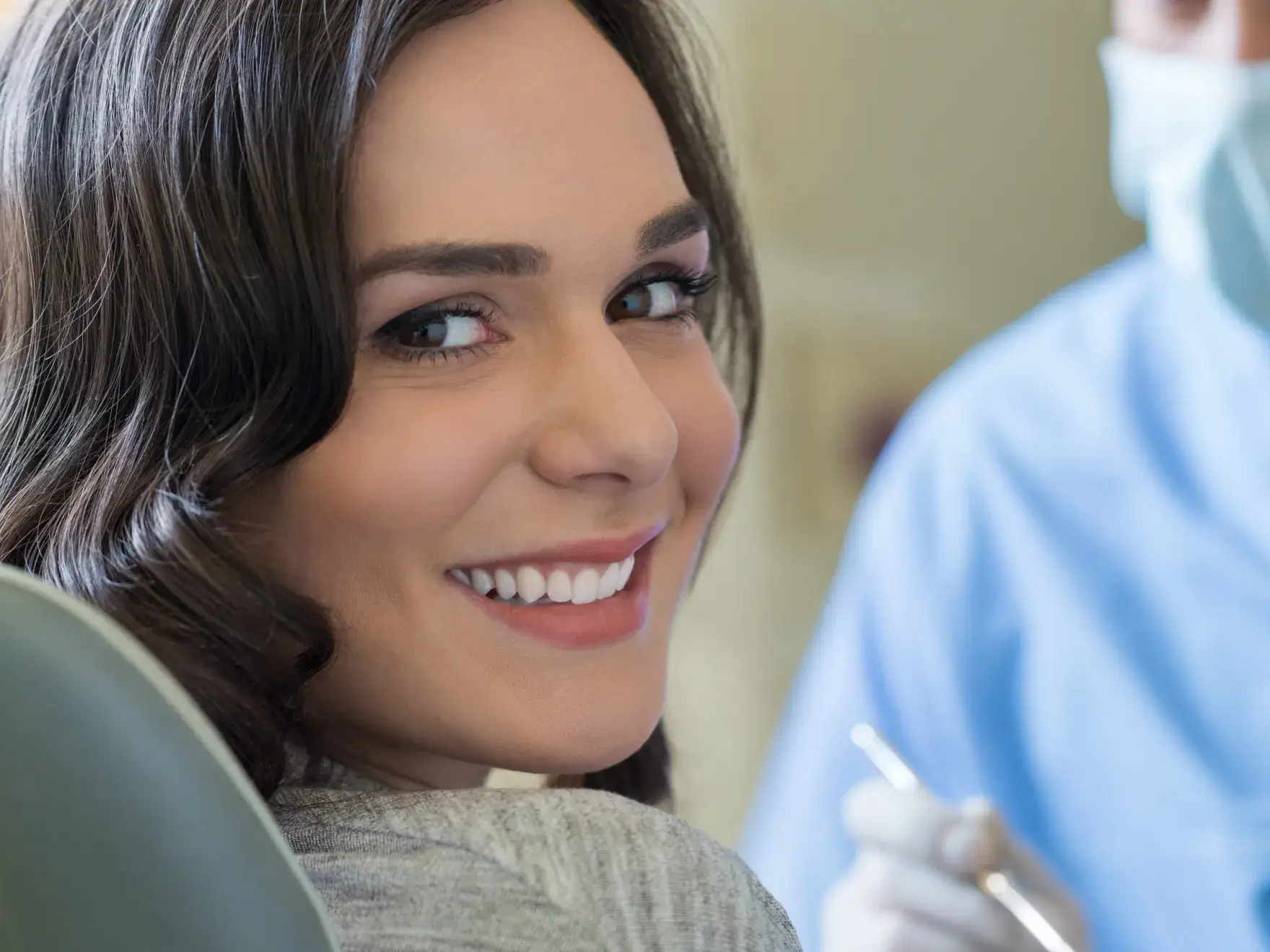 A woman is sitting in a dental chair, smiling back at the camera.