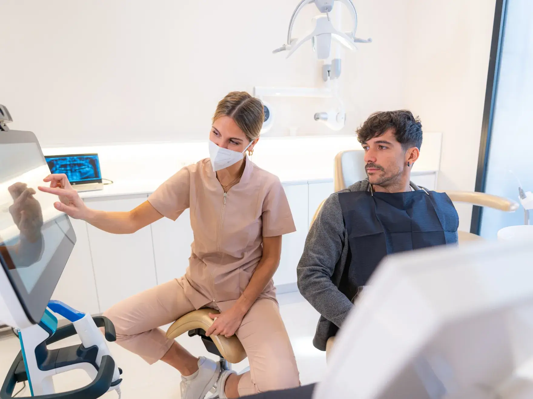 A dentist shows a patient something on a touchscreen monitor in a dental office.
