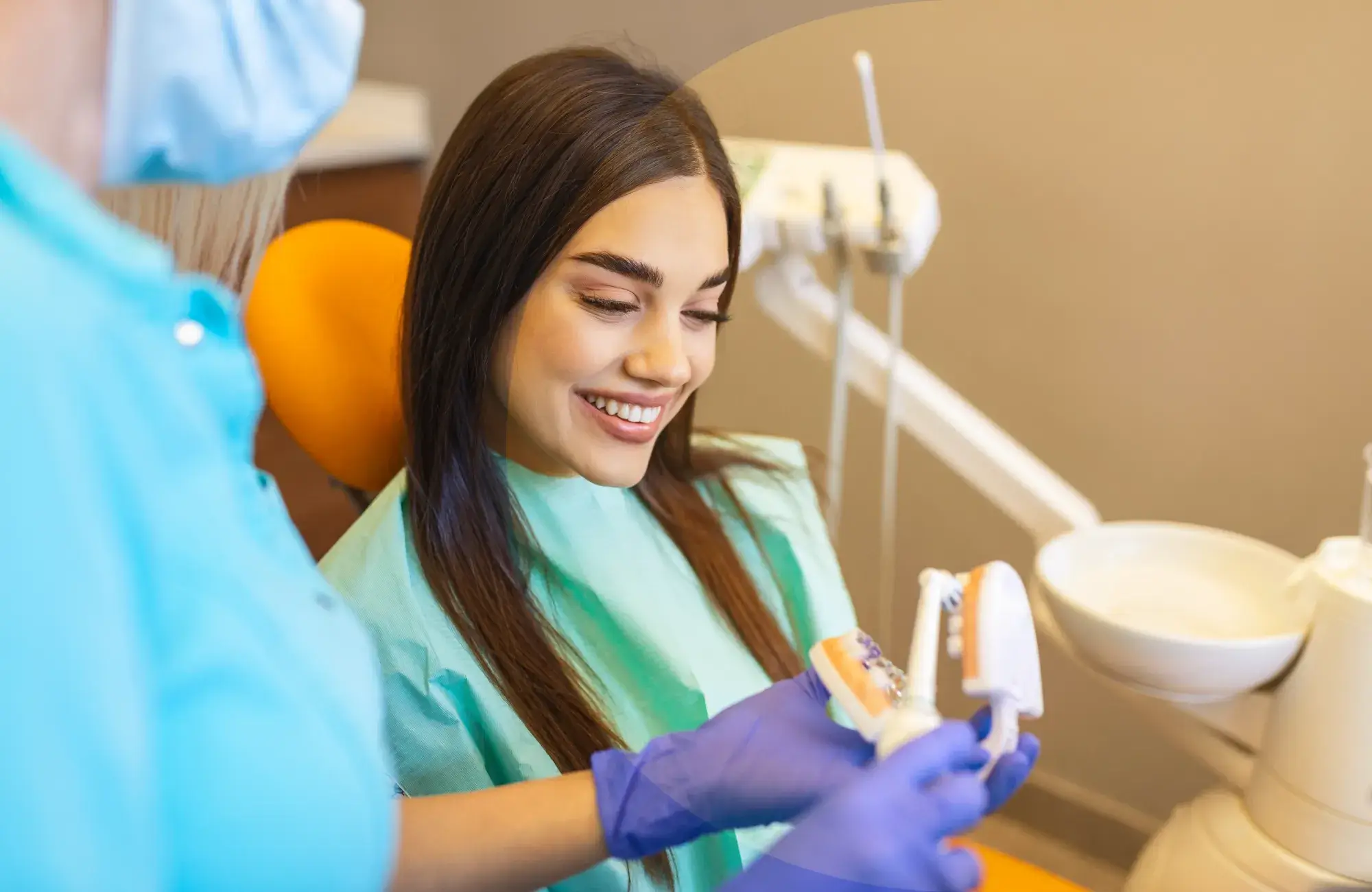 Dentist shows a smiling woman a dental model while she sits in the examination chair.