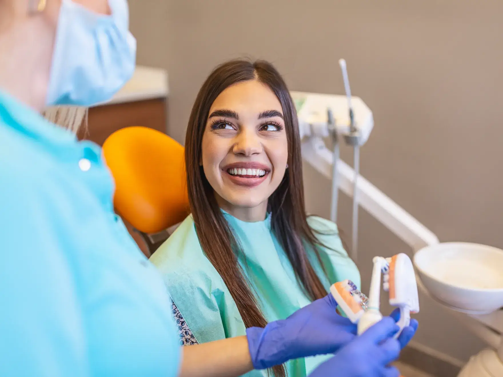 A woman at a dental clinic smiles while a dentist shows her a dental model.